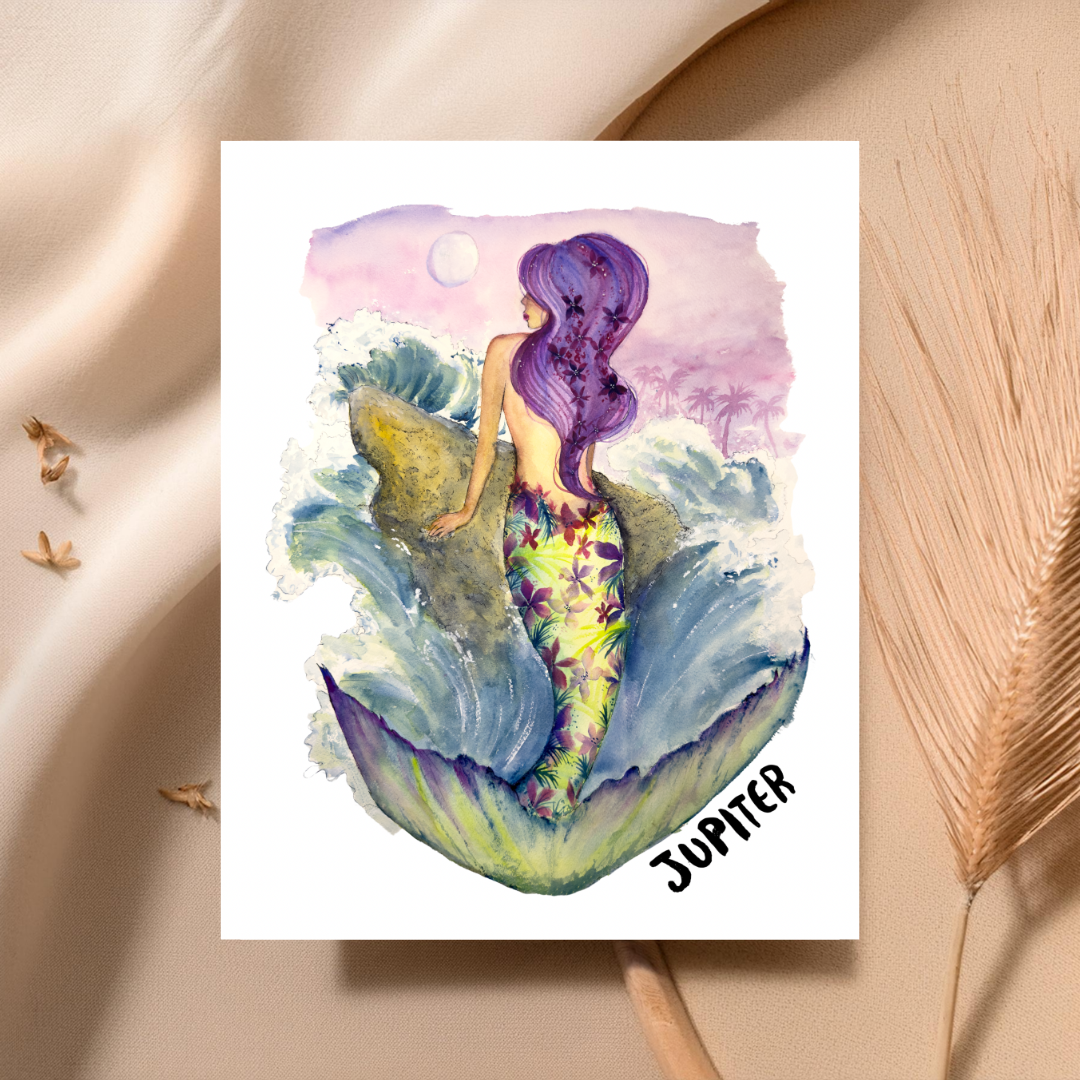 A watercolor art print of a mermaid labeled 'JUPITER' with purple hair and a green-yellow tail, styled on a beige fabric background with dried wheat stalks.